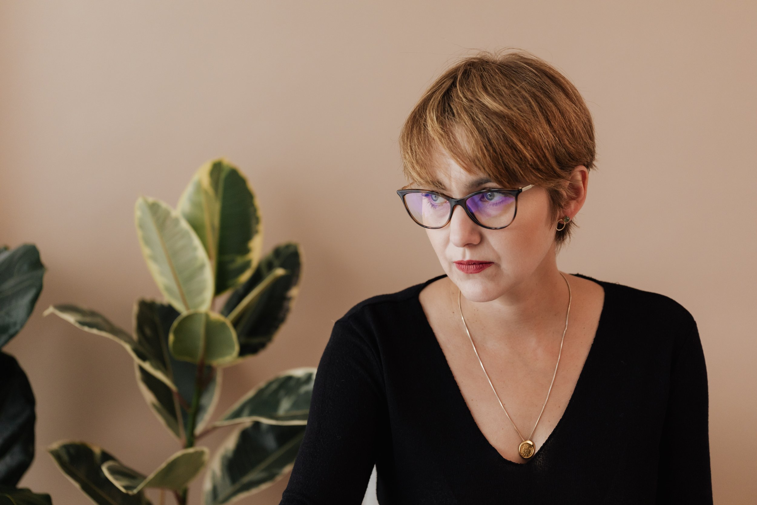 A woman with short hair and glasses working at a desk beside a large rubber plant